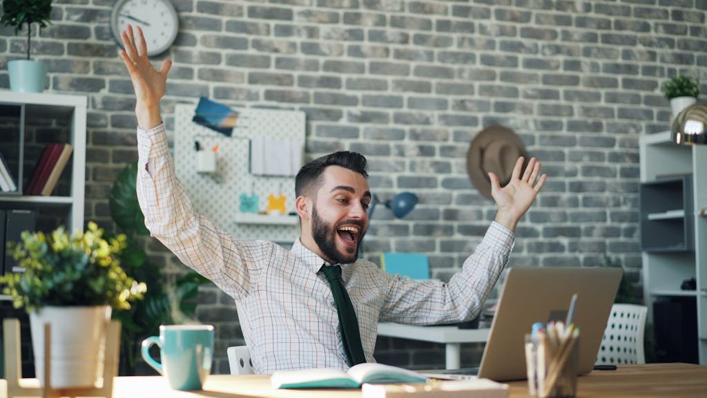 A delighted office worker celebrating success at his desk in a modern office setting. Ecommerce Keyword Research Tutorial.
