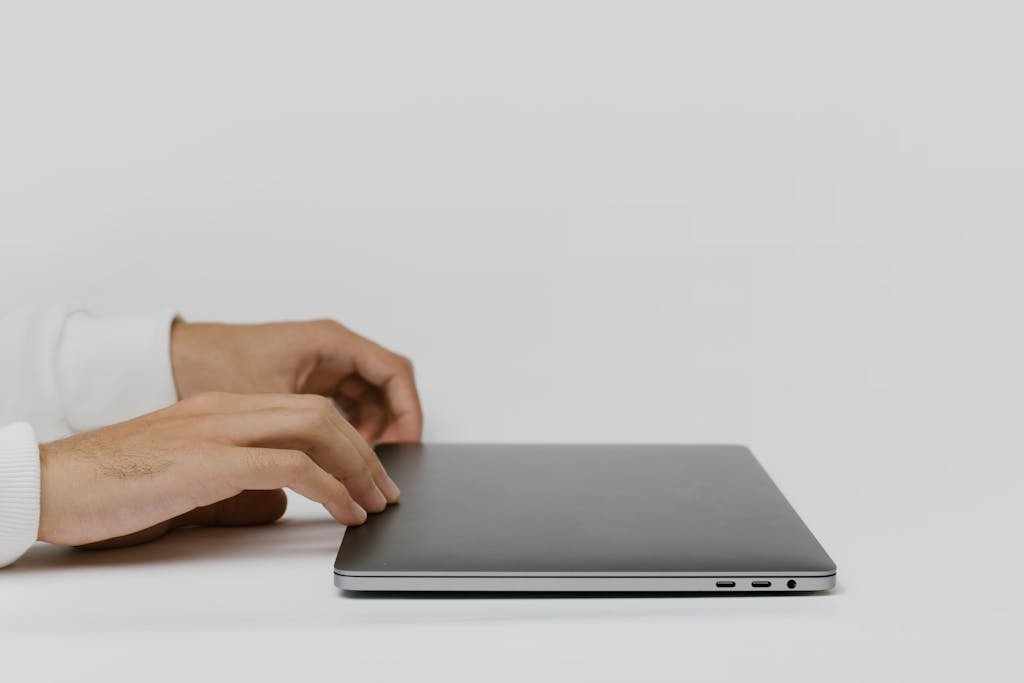 Hands preparing to open a closed laptop on a minimalist desk, ready for work. Programmatic SEO for Shopify