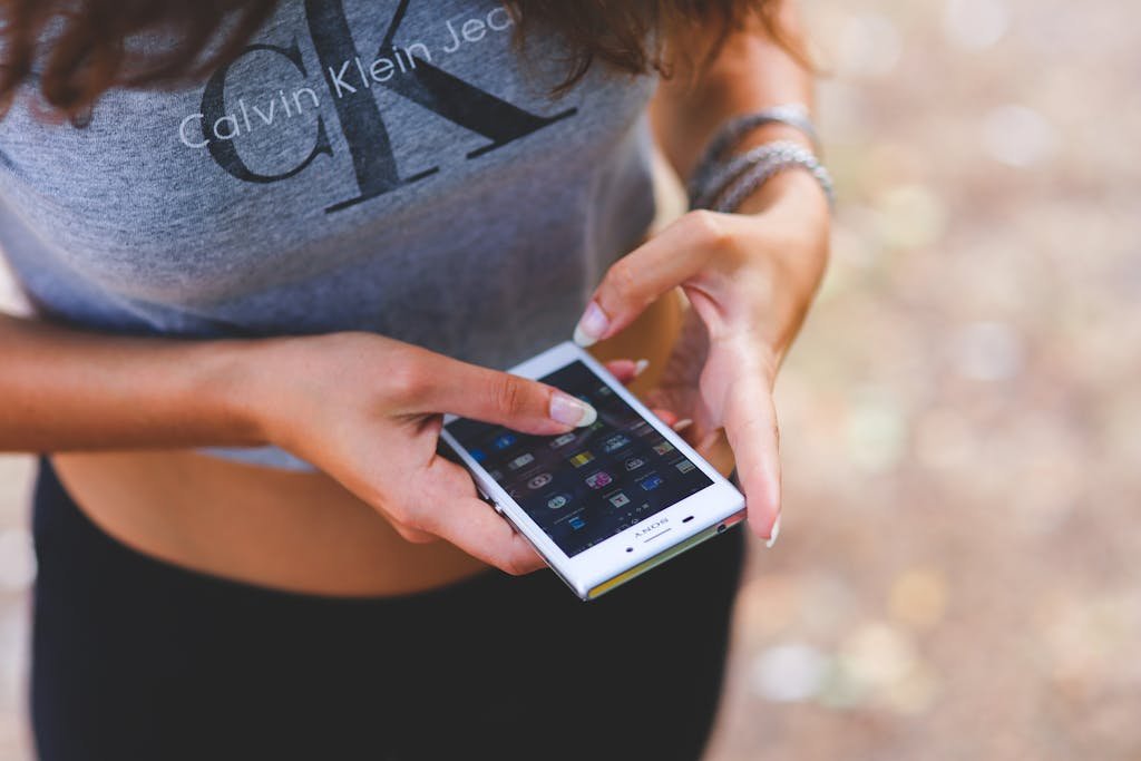 Young woman interacting with smartphone outdoors, wearing casual crop top.
